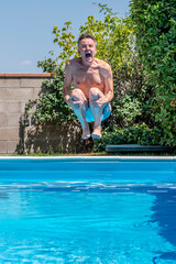 Caucasian man with a funny expression takes a cannonball bomb dive in the swimming pool on a sunny...