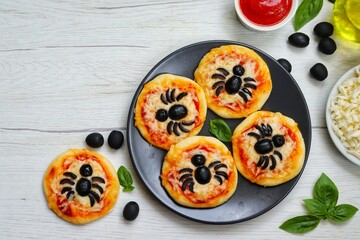 Halloween mini spider pizzas made from pizza crust,puzza sauce,mozzarella cheeses and black olives on plate with white wood table background.Art food idea for kids Halloween party.Copy space