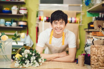 Fototapeta premium Male florist in flower shop. Man in apron is cutting stems and preparing roses for a bouquet. Owner of the flower shop, doing small business.
