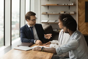 Caucasian family financial advisor consulting to young 30s African couple during meeting in bank...