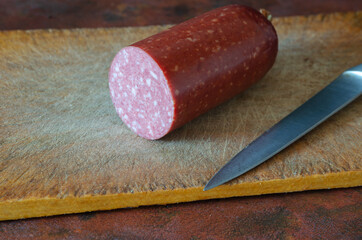 Salami and a kitchen knife on a red countertop. Half of a sausag
