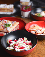 A lot of different dessert in plates on a wooden table. Strawberry puff pastry, panna cotta, cheesecake.