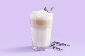 Glass of tasty lavender latte and flowers on color background