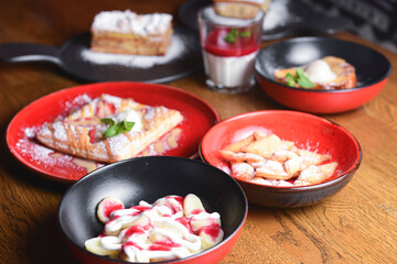 A lot of different dessert in plates on a wooden table. Strawberry puff pastry, panna cotta, cheesecake.