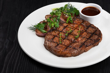 Grilled black angus steak ribeye on white plate on black wooden background