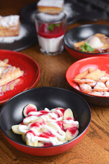 A lot of different dessert in plates on a wooden table. Strawberry puff pastry, panna cotta, cheesecake.