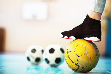 A human foot rest on the football on the concrete floor. Photo of one soccer ball and sneakers in a...