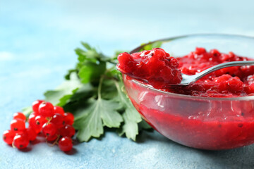 Bowl tasty red currant jam, berries and leaves on color background, closeup