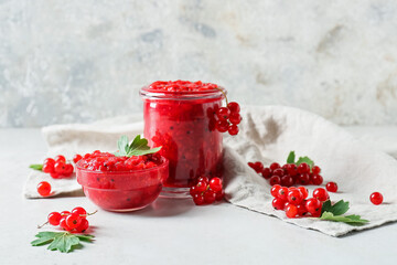 Bowl and jar of tasty red currant jam on light background