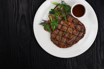 Grilled black angus steak ribeye on white plate on black wooden background