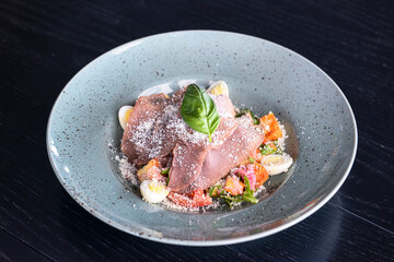 Fresh summer salad with stripes of beef, tomatoes, eggs, fresh arugula, basil and cheese on top.