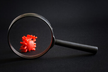 Toy virus under a magnifying glass against a black background. The concept of studying new viruses,...