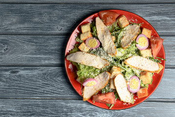 Caesar Salad made of chicken meat, tomatoes, eggs, fresh arugula, croutons, cheese and sauce on top.