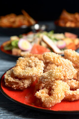 Golden onion rings and sauce in a saucepan served on a red plate. Over dark black background.