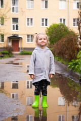 Fototapeta na wymiar Portrait of little girl in rubber boots in puddle
