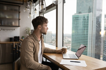 Thoughtful businessman contemplating looks at big city modern skyscrapers district view through...