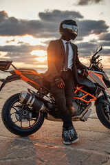 Man dressed in suit and helmet posing on beach with bike