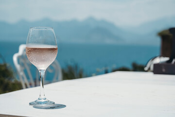 A glass of rose wine on the table of a street cafe against the background of the Mediterranean sea and blue sky on a sunny summer day. Summer, travel, lifestyle, relaxation, and enjoyment concept.