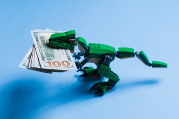A pack of 100 dollar bills in mouth of tyrannosaur green kid toy isolated on blue background. Copy space. Concept of a unique advertising and design.