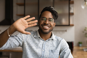 Handsome smiling African stylish hipster guy in glasses wave hand greet friend start video...