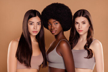 Photo of adorable serious three best friends wear cropped tops embracing isolated beige color background