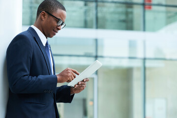 Handsome smiling young marketing manager standing outdoors with tablet computer and reading news on digital tablet