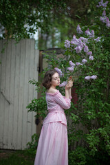 beautiful young girl, a brunette in a pink dress walks in the lilac garden, a peasant woman in the village