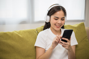 Relaxing time on sofa. Beautiful young asian woman sitting on sofa she choose music from smartphone take a rest and listening song with headphone. Lifestyle in living room at house in the morning.