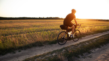 Bike traveler riding through the field at sunset on bicycle with bags