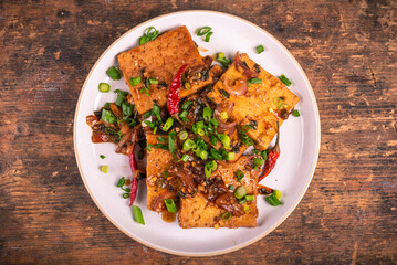 Fried tofu with onions and hot peppers, sprinkled with green onions on a grater, top view