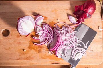 Sliced red onion and a large knife on a wooden kitchen board - morning in the kitchen