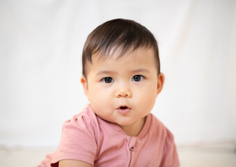 An Asian girl about 1 year old. Playing in the living room in the house. A cute baby wearing a pink dress Stay with parents in the house