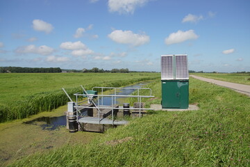 Very small Dutch weir (Dutch: valve weir) with solar panels near a ditch. The weir regulates the water drainage capacity of the surface water body. Summer, meadows, August. Netherlands