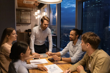 Confident male leader brainstorming working until late in modern office boardroom with multi racial...