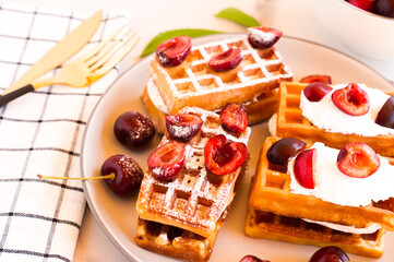 traditional Belgian waffles with fresh cherries and cream on a plate. close up.