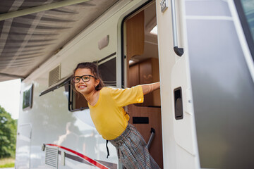 Happy small girl standing by caravan door, family holiday trip. - obrazy, fototapety, plakaty