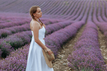 A beautiful young woman in a white dress with a hat walks through a lavender field