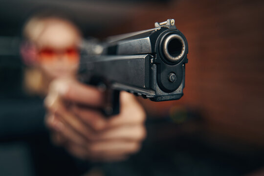 Blonde woman in protective eyewear firing a handgun