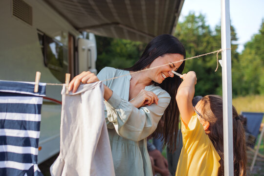 Mother With Daughter Hanging Clothes By Car Outdoors In Campsite, Caravan Family Holiday Trip.