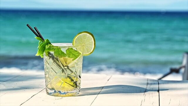 Cocktail with ice, slice of lime, aegean sea on the background, Greece. Slow motion