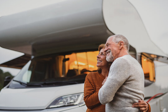 Senior Couple Standing And Hugging Outdoors At Dusk, Caravan Holiday Trip.