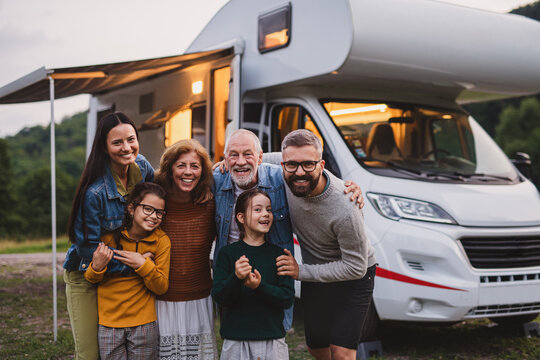 Multi-generation family looking at camera outdoors at dusk, caravan holiday trip.