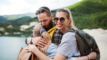 Happy family with preteen daughter on hiking trip on summer holiday, resting and hugging.