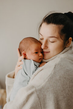 Loving mother carying of her newborn baby at home. Bright portrait of happy mum holding cute infant child on hands. Mother hugging her little 1 months old daughter.