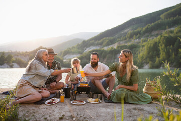 Happy multigeneration family on summer holiday trip, barbecue by lake.