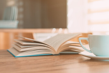 Open book and coffee cup on the table, reading at home in the morning