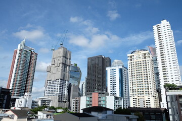 Six high buildings with modern architecture and one buildings under construction with crane against blue sky background and surrounded by houses.