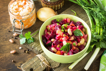 Beetroot salad vinaigrette with sauerkraut, pickled cucumber and vegetables on a wooden rustic table.