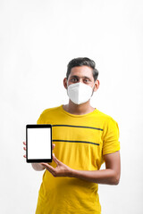 young indian man wearing mask and showing tablet