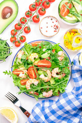 Shrimp salad with cherry tomatoes, arugula, avocado, and oil lemon dressing on white background. Top view